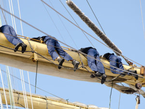 Team of yacht crew in blue trousers preparing main sail